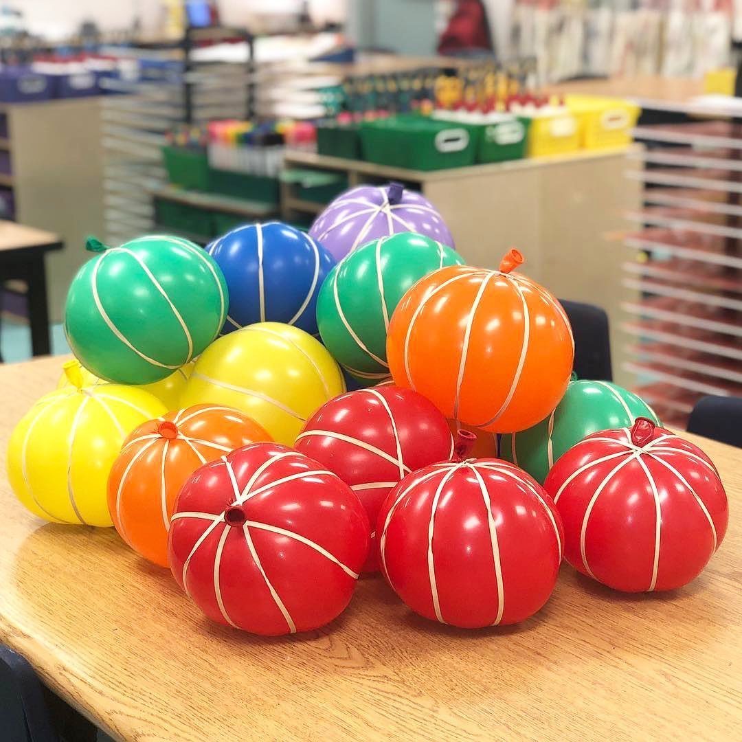 Colorful balloons wrapped in white string to look like pumpkins on a table.