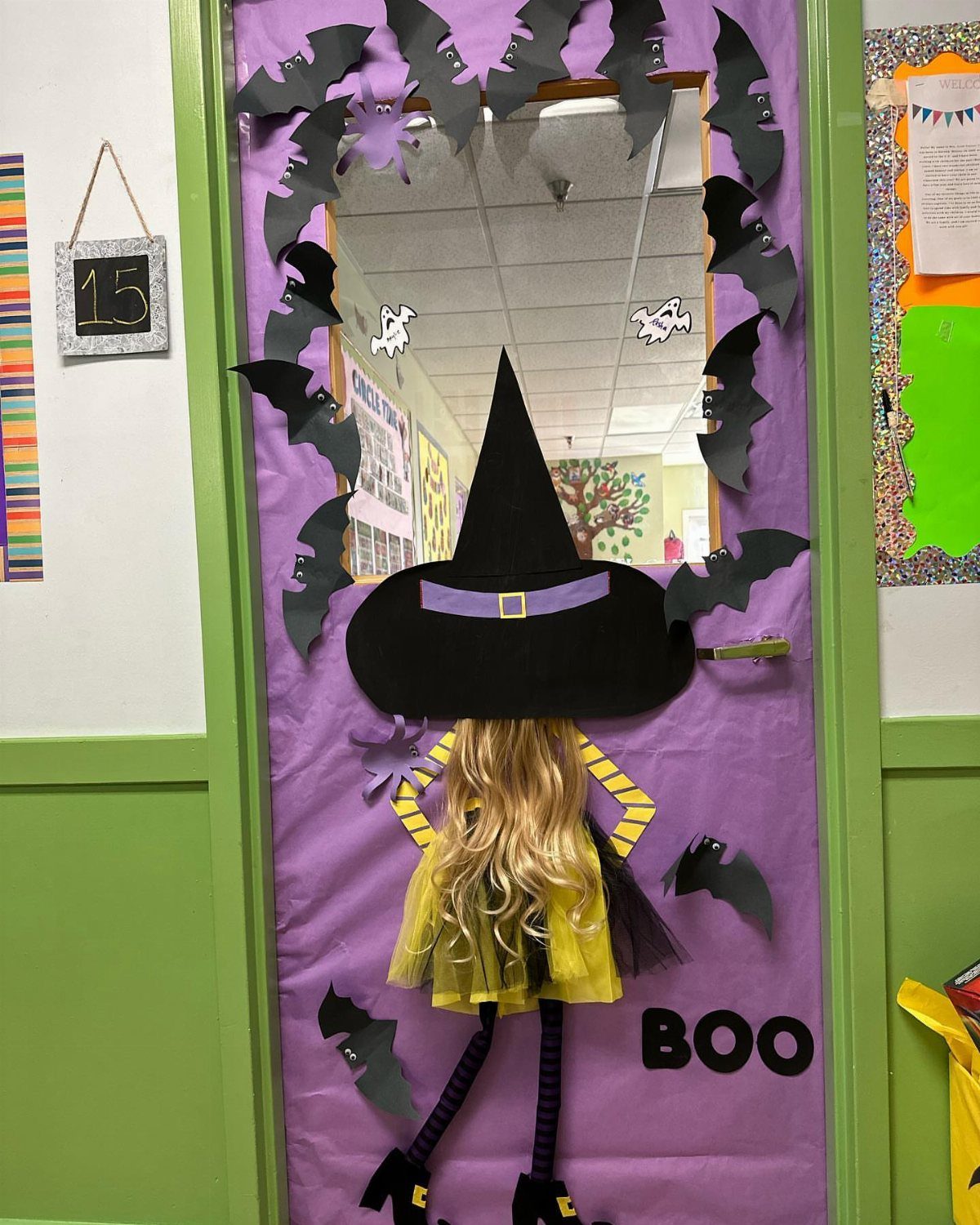Witch figure and black bats decorating a purple classroom door for Halloween.