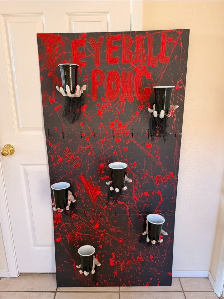 Eyeball Pong game board with black cups held by zombie hands and red splatters.