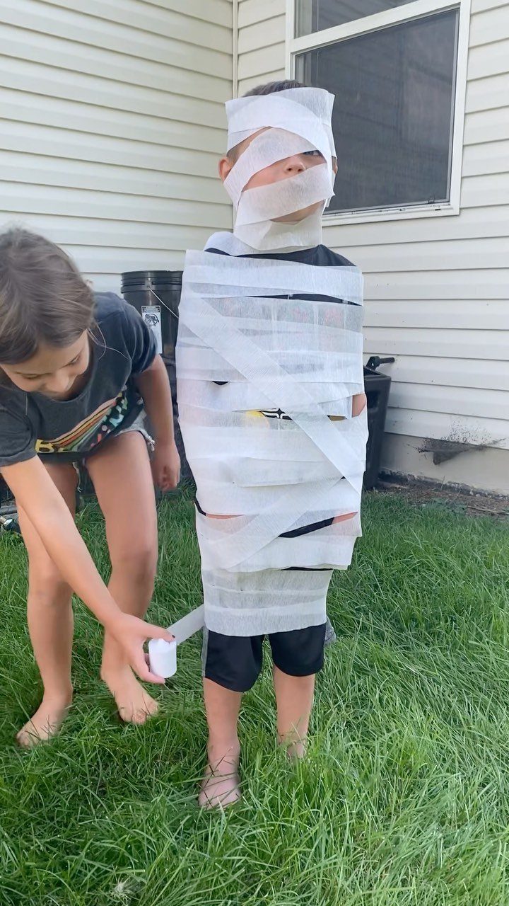Girl wrapping a boy in toilet paper to look like a mummy outdoors