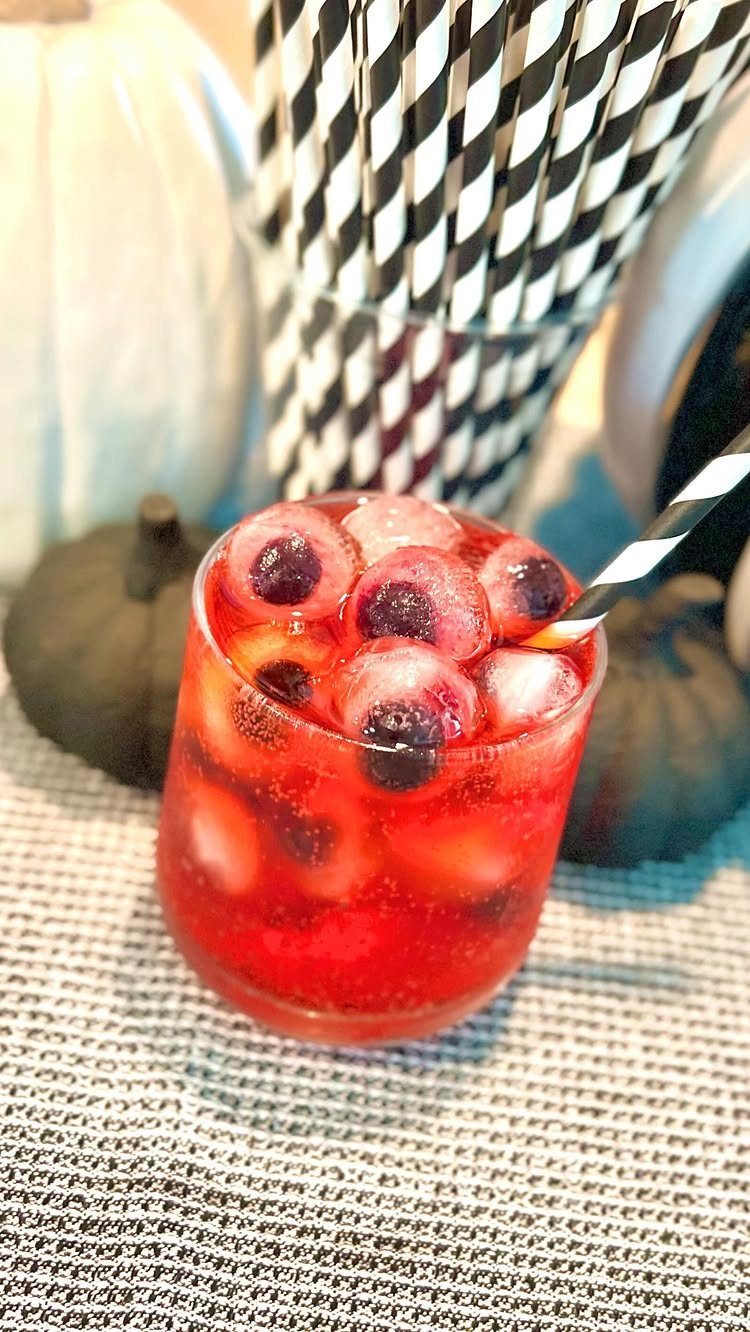 Red cocktail with eyeball ice cubes and striped straw near Halloween pumpkins