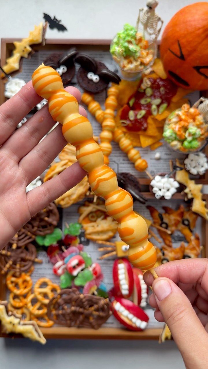 Hands holding a skewer of glazed donut holes over a Halloween snack tray.