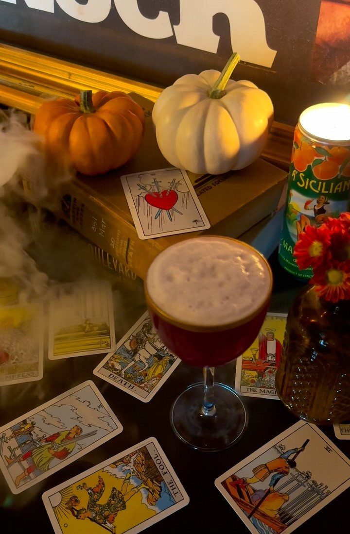 Tarot cards and a red cocktail surrounded by pumpkins and a candle.