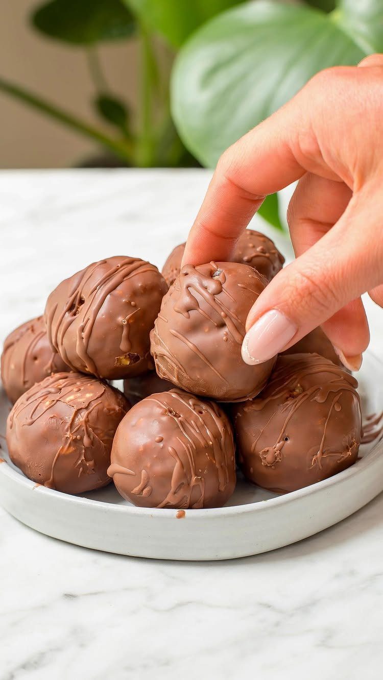 Chocolate covered truffles on a grey plate with a hand picking one up.