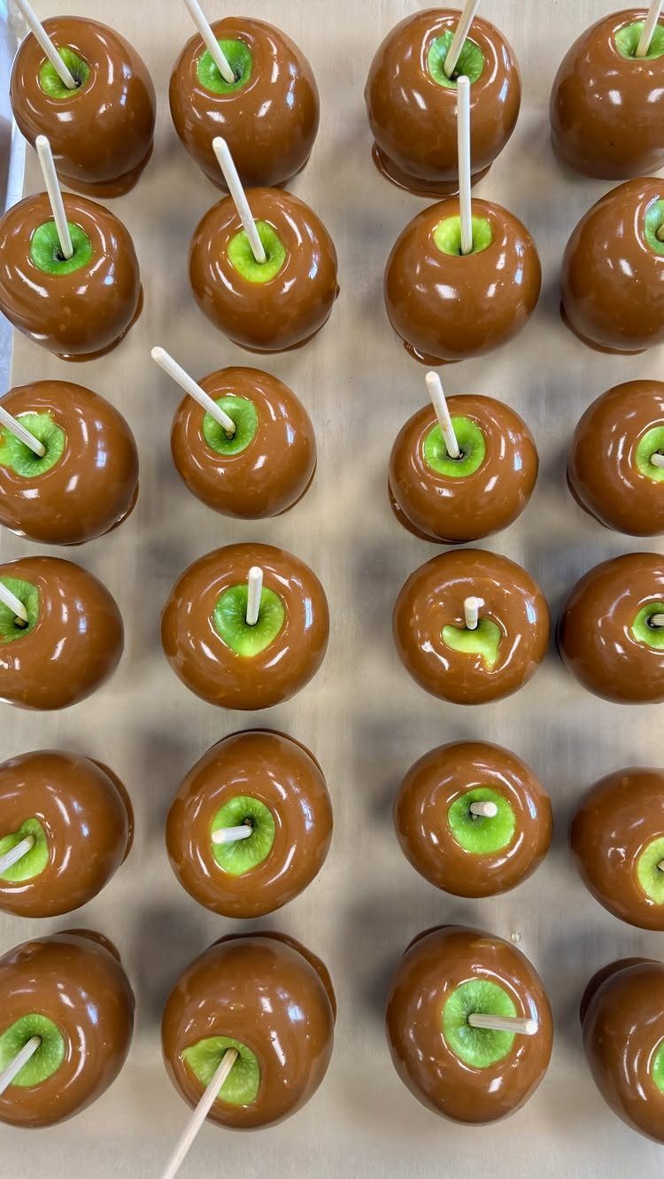 Caramel coated green apples with wooden sticks arranged in neat rows.
