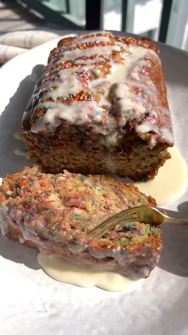 Banana bread loaf with white icing and sprinkles on a white plate.