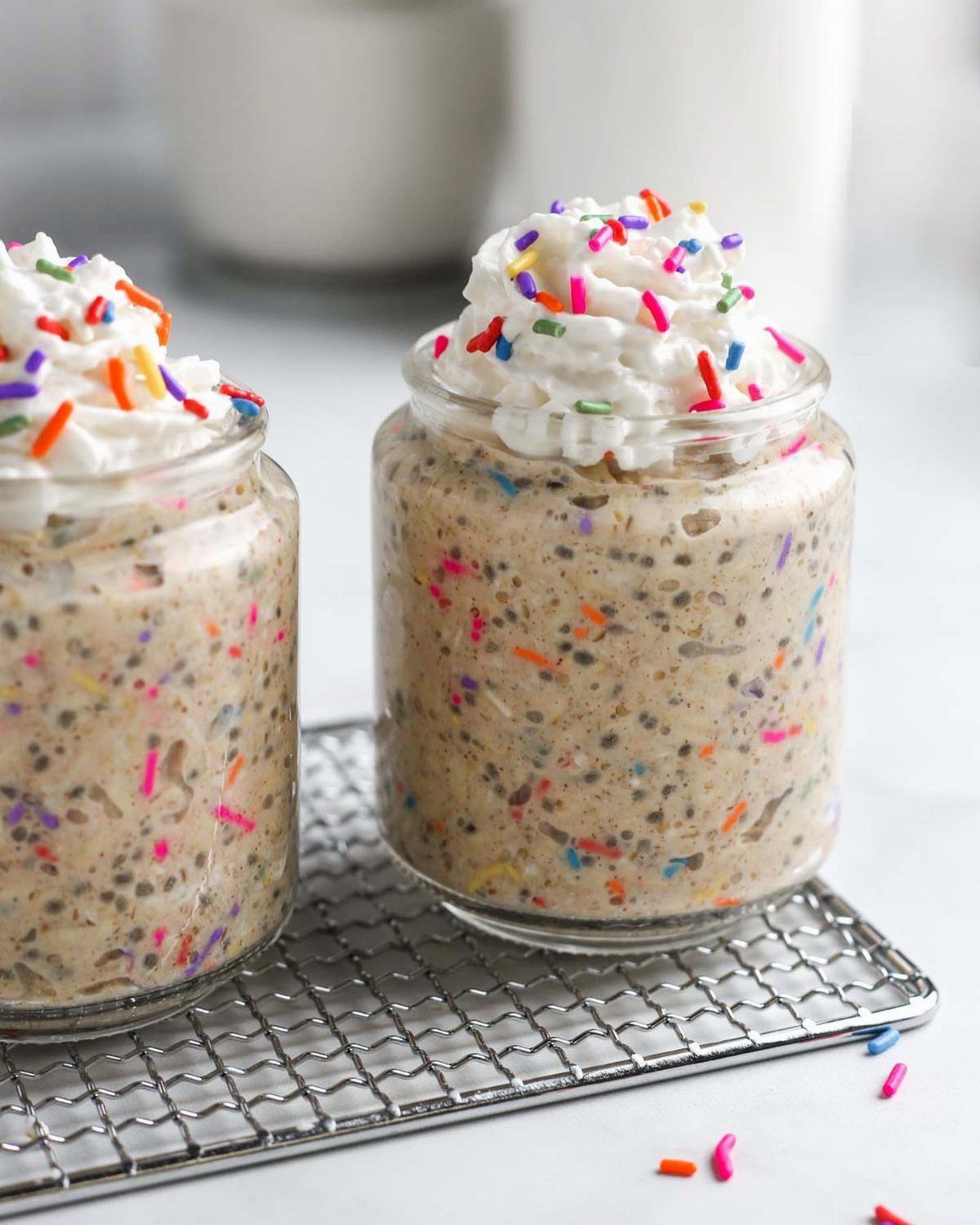 Two jars of birthday cake overnight oats topped with whipped cream and sprinkles.