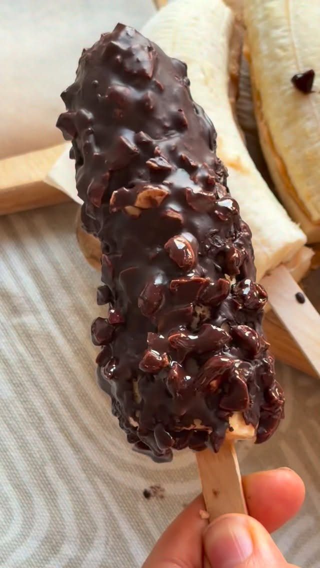 Chocolate covered frozen banana on a stick topped with crushed nuts.
