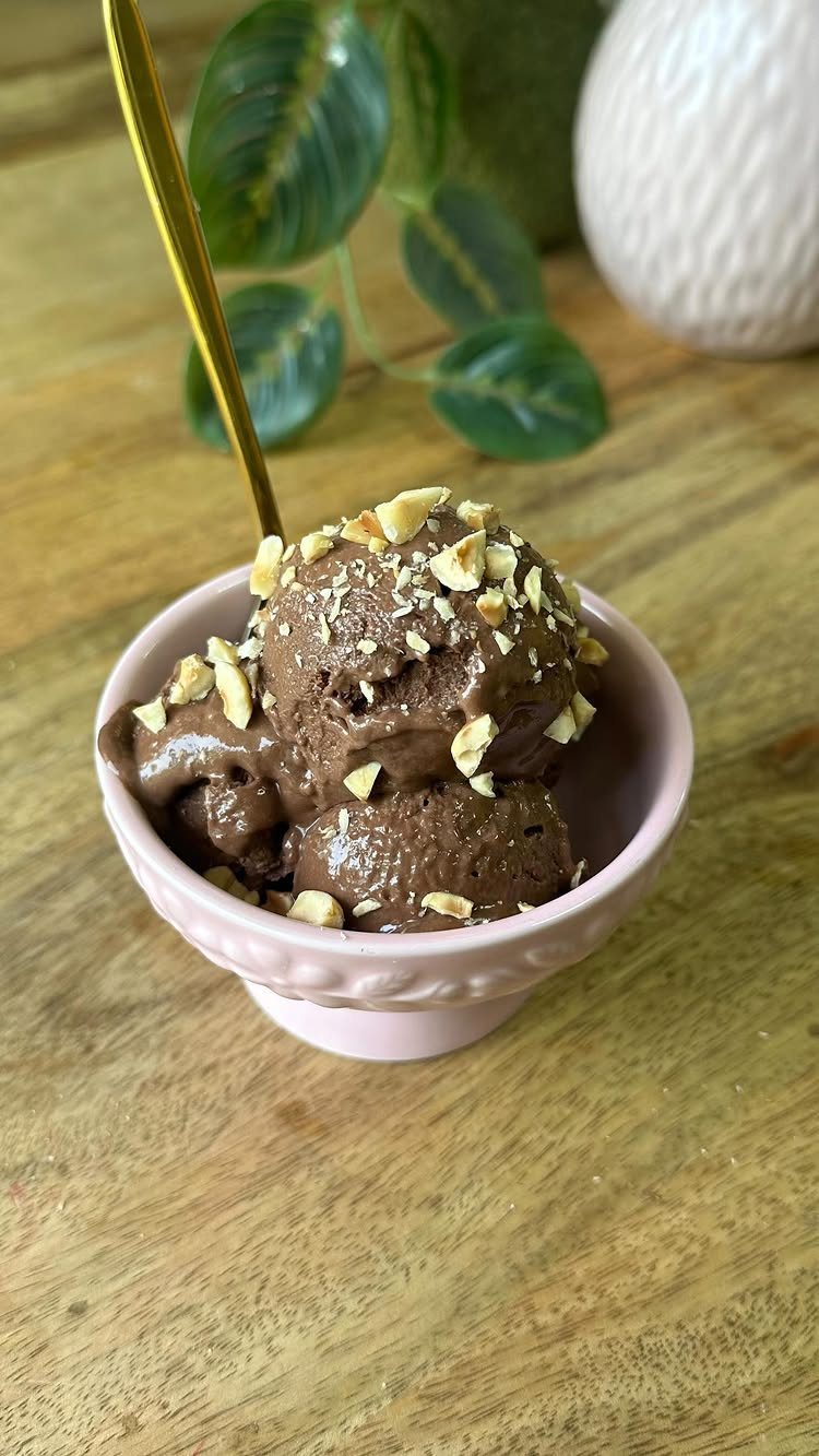 Chocolate ice cream with chopped nuts in a small pink bowl on wood.