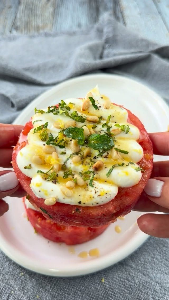 Watermelon slice topped with white cream, lemon zest, mint, and pine nuts.