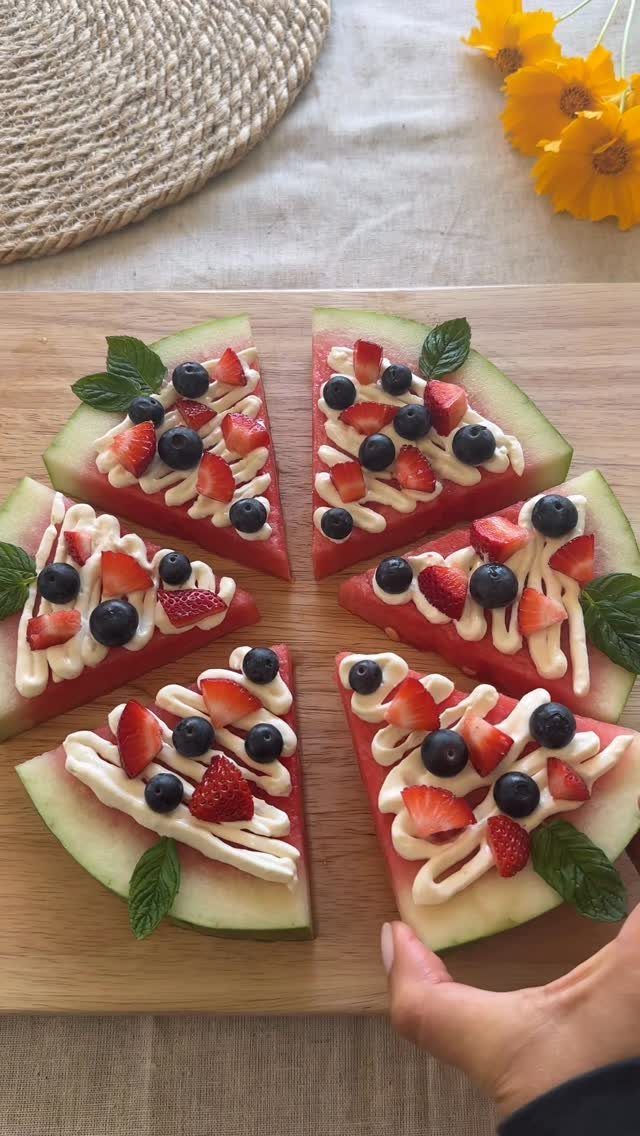 Watermelon pizza slices topped with white cream, blueberries, strawberries, and mint leaves.