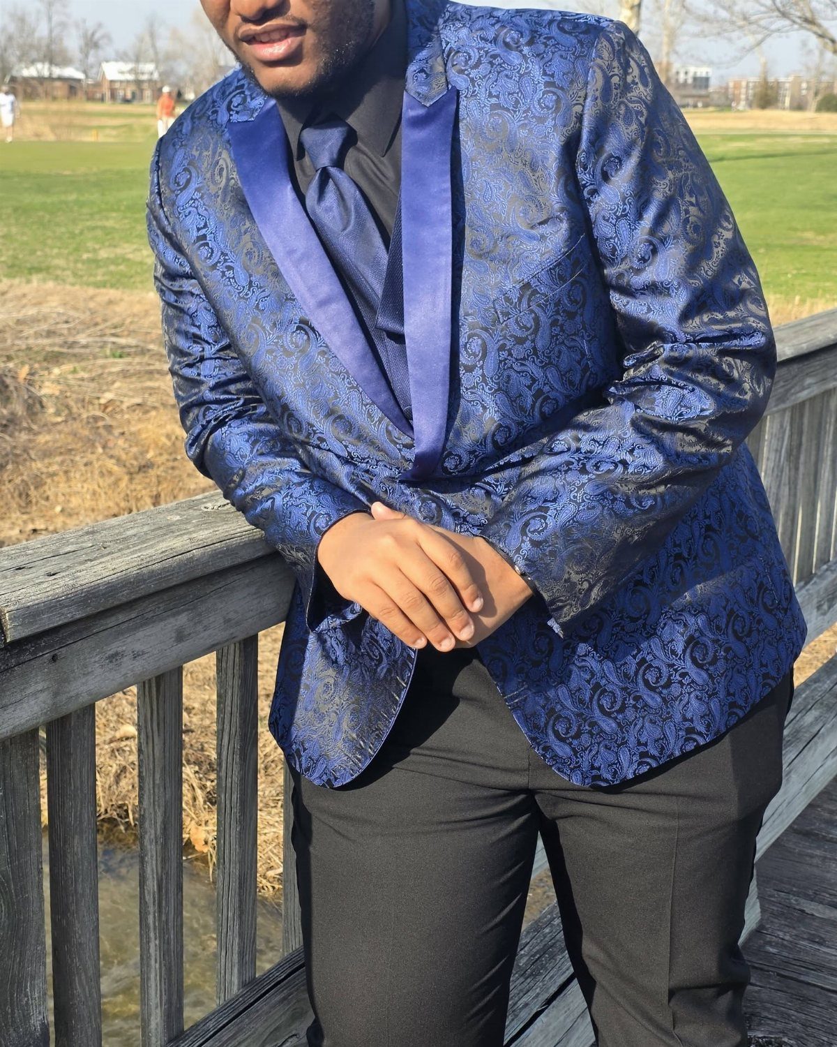 Man in a royal blue patterned blazer and black pants on a wooden bridge.