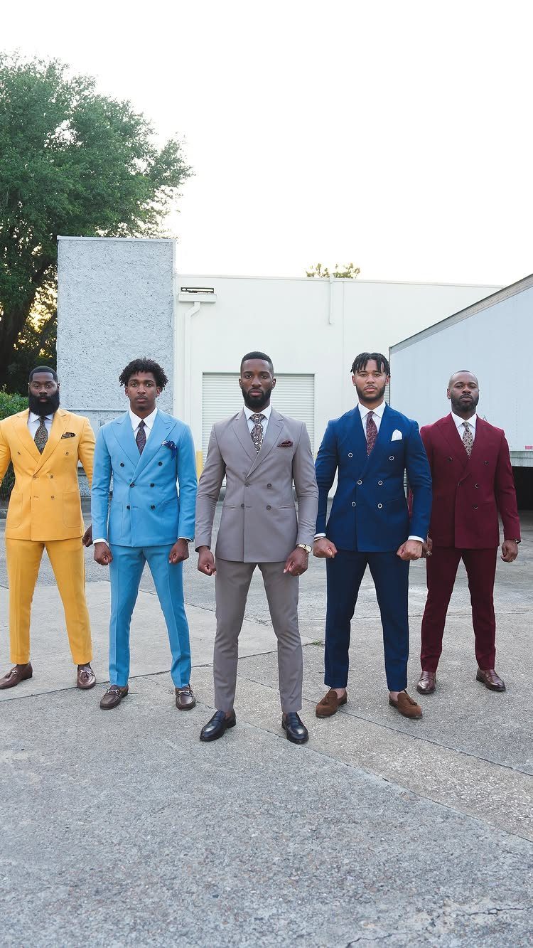 Five men posing in colorful tailored suits including yellow, blue, grey, and burgundy.