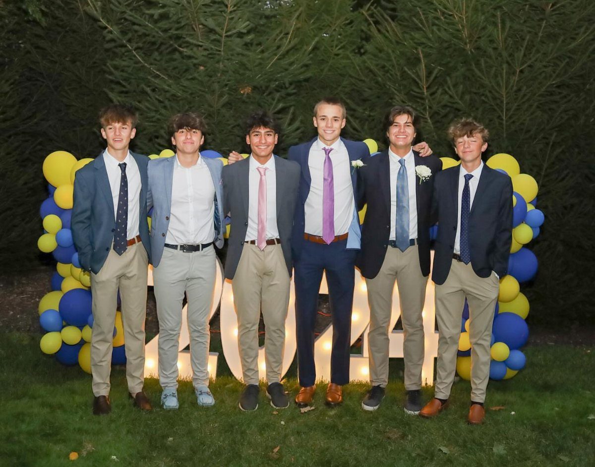 Six young men wearing blazers and chinos posing by a balloon arch.