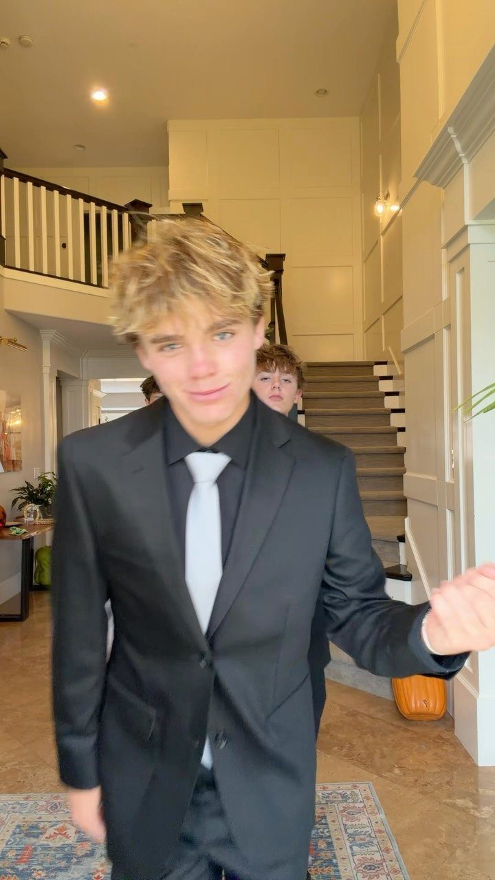Young man in a black suit and light tie posing in a home hallway