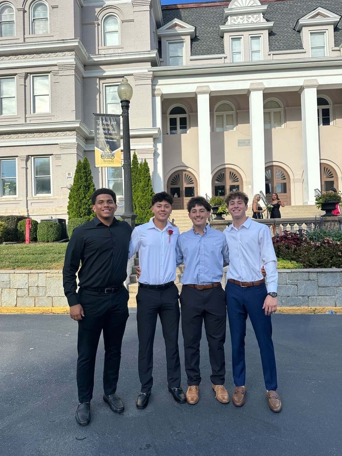 Four young men in dress shirts and trousers posing before a grand building.