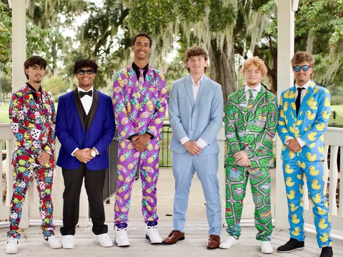 Six young men posing in colorful, patterned and classic suits on a porch