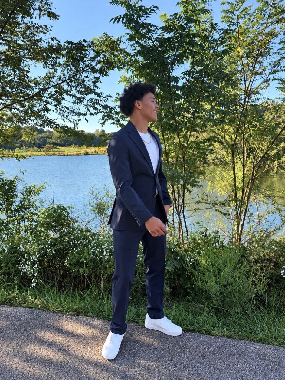 Young man in a navy blue suit and white sneakers posing by a lake