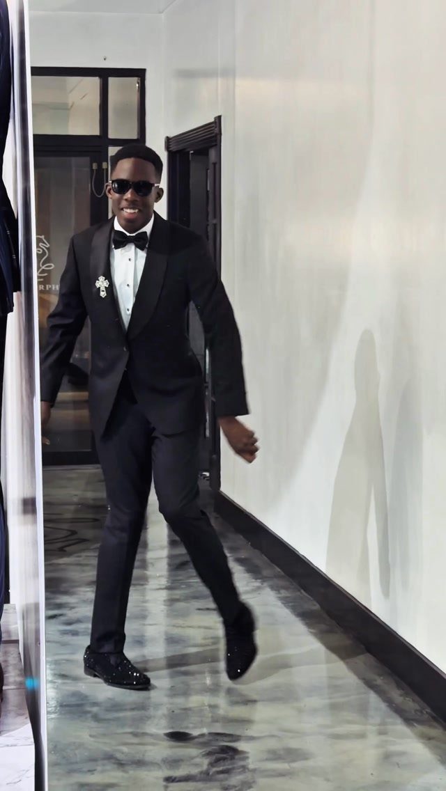 Man in a black tuxedo and sunglasses walking through a white hallway
