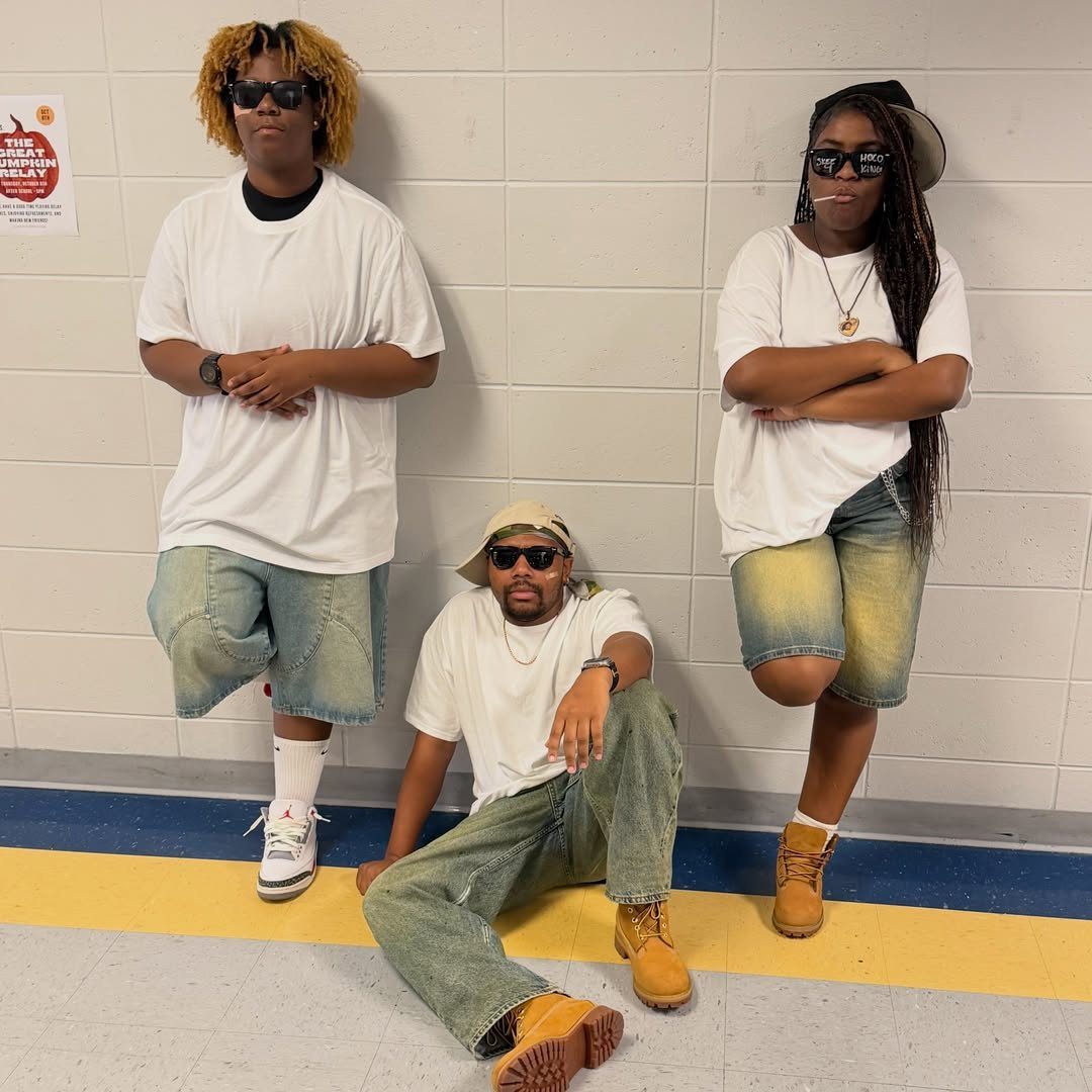 Three students in 90s style oversized white shirts and baggy denim posing together.
