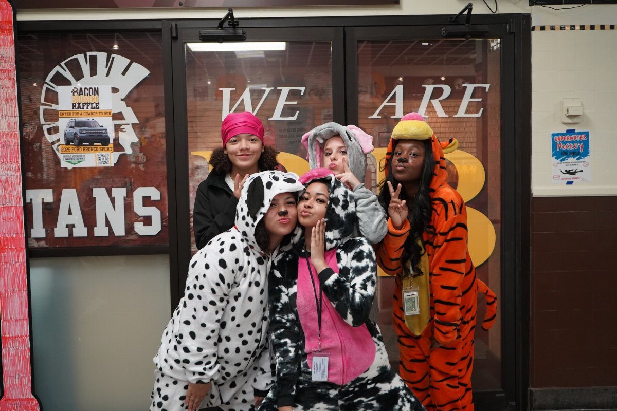 Five teenage girls wearing animal onesies posing together in a school hallway.