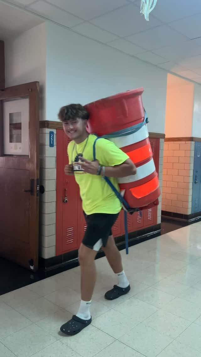 Teenage boy carrying a large red and white traffic barrel in a school hallway