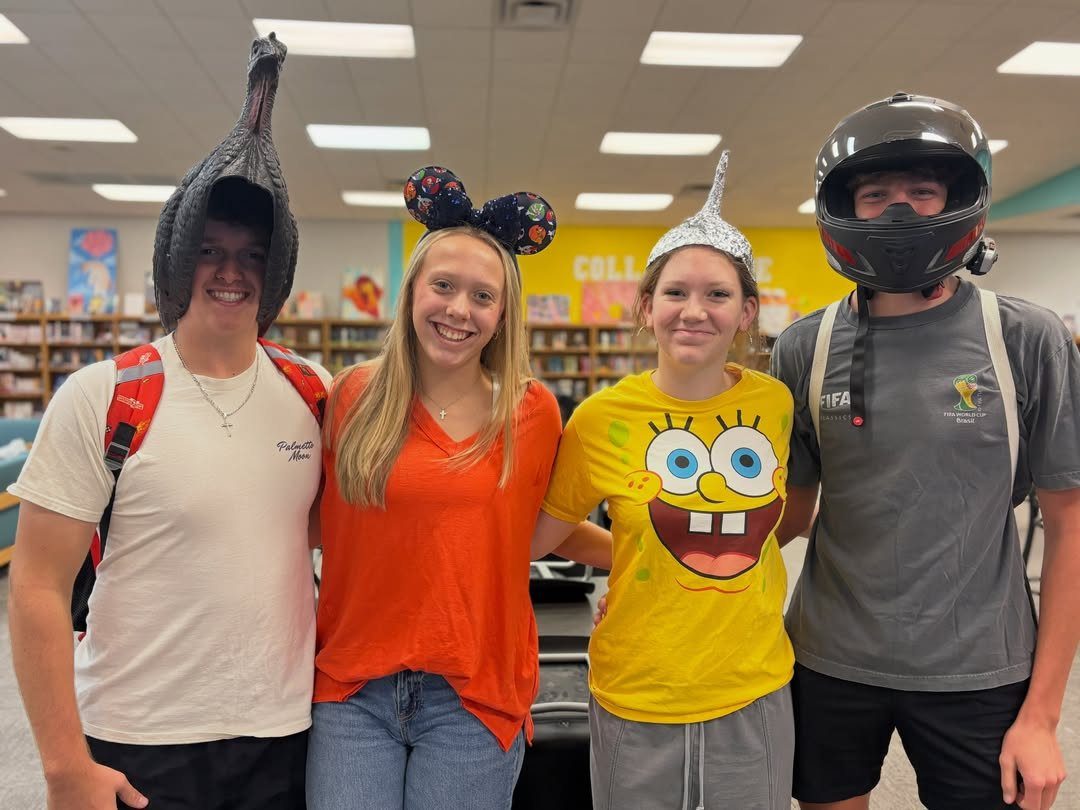 Four students wearing a fish head, mouse ears, a cone, and a helmet.