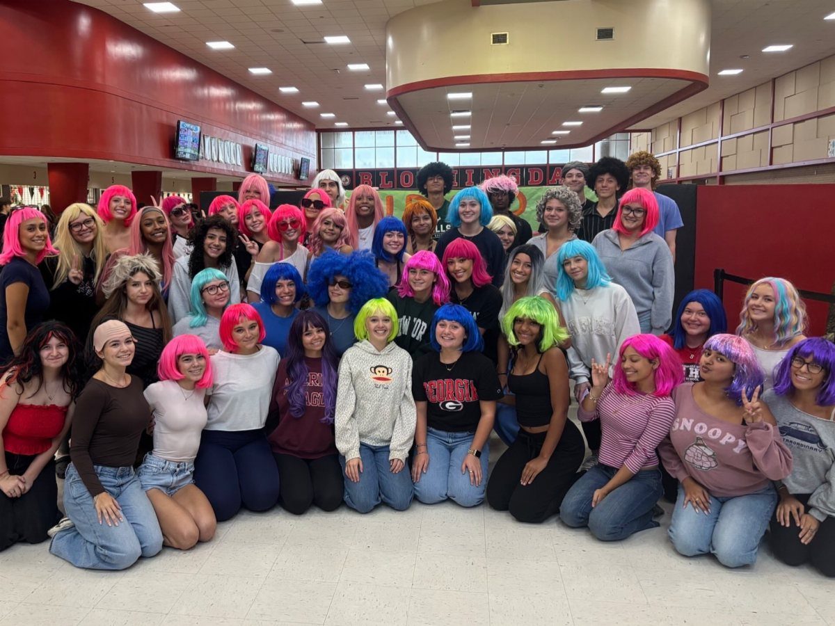 Group of teenage girls wearing colorful wigs posing together in a school hallway.