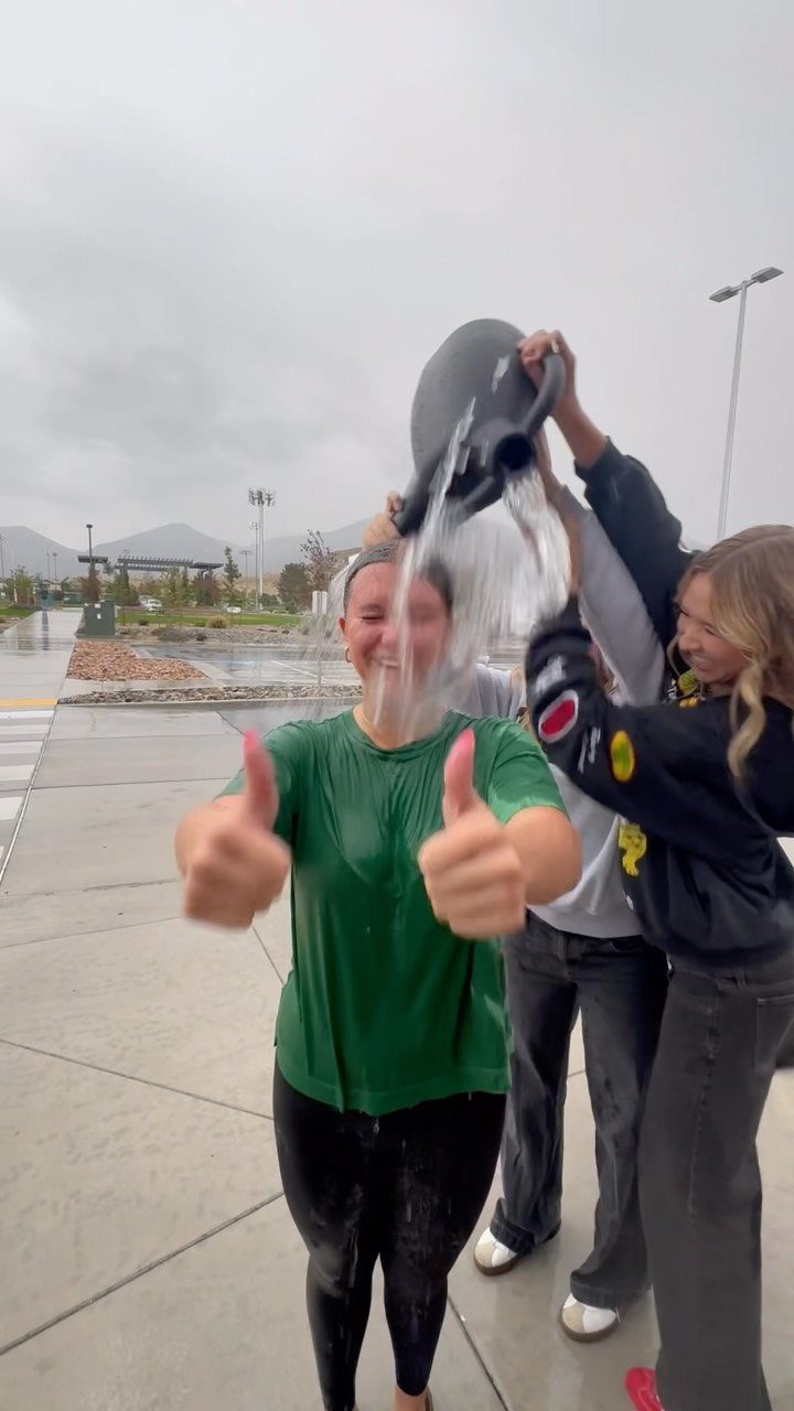 Young woman in green shirt getting water poured over her head outdoors.