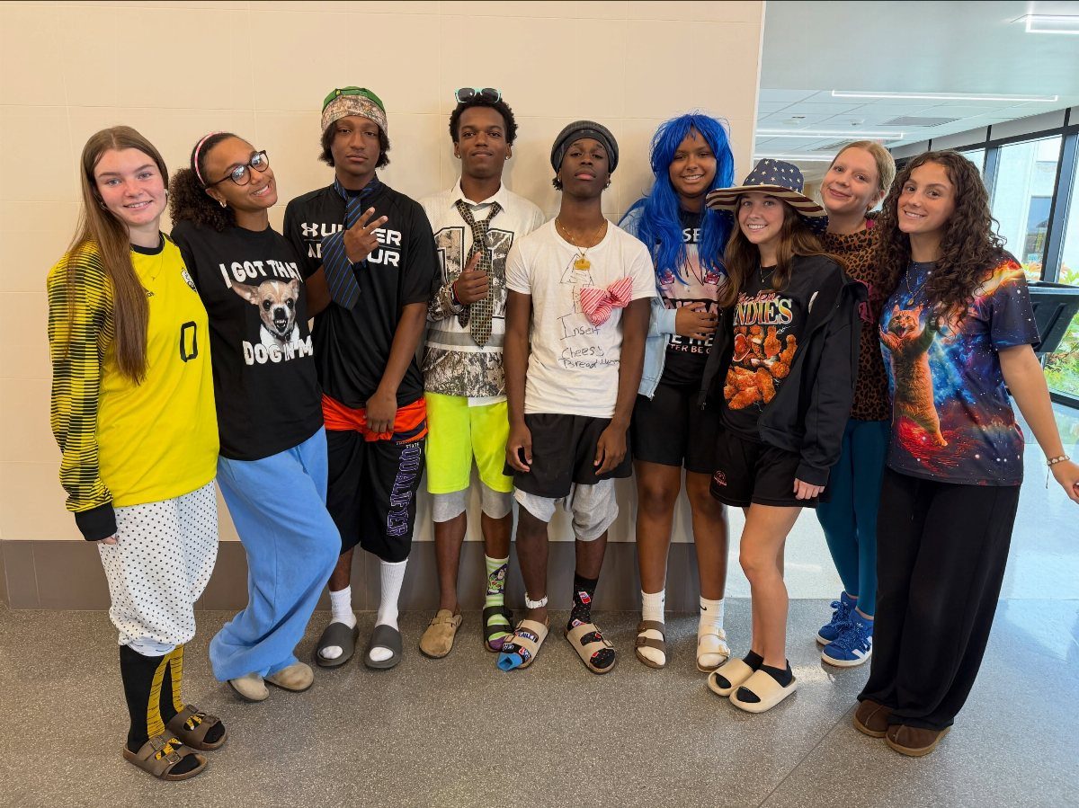 Group of teenagers in mismatched, eclectic outfits posing in a school hallway.