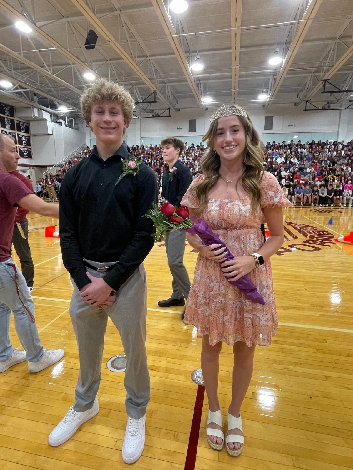 Teenage boy and girl in formal attire posing in a school gymnasium.