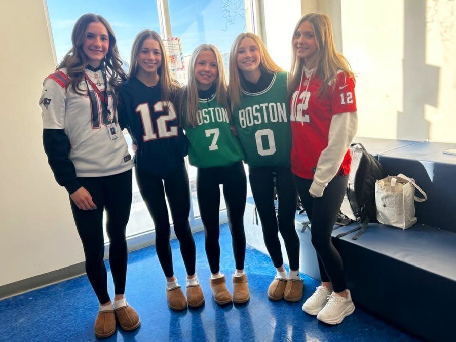 Five teenage girls posing in sports jerseys and black leggings in a school hallway.