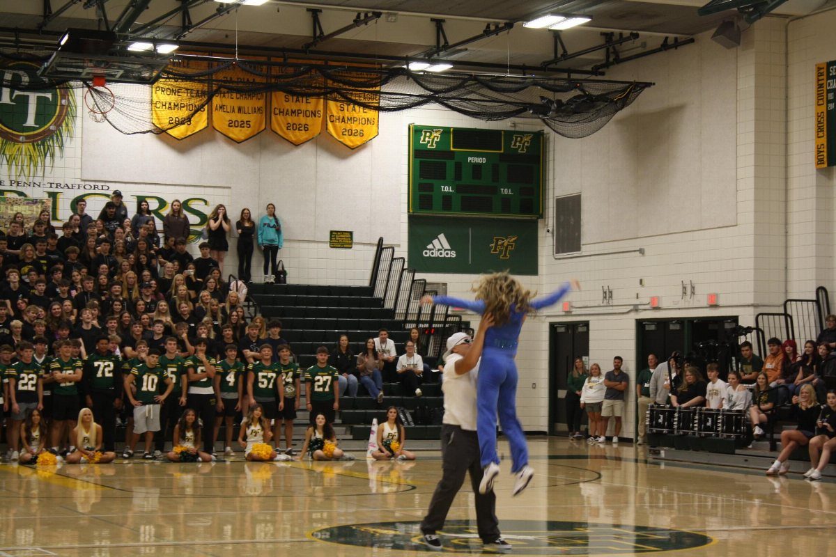 Cheerleader being lifted in a gym with students and football players watching