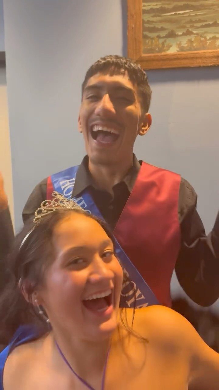 Young man and woman wearing sashes and a tiara, smiling for a photo.