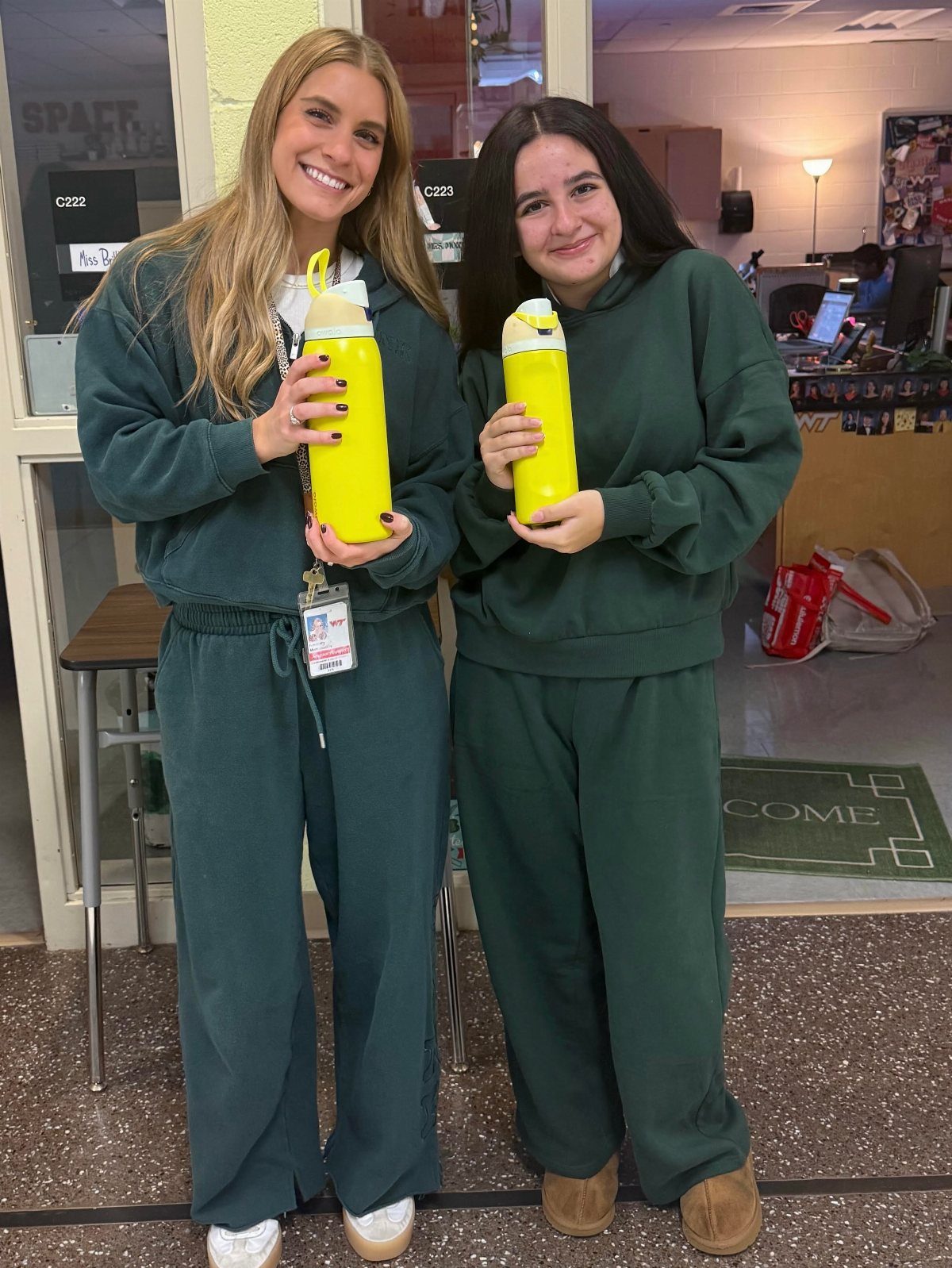 Two students wearing matching dark green outfits and holding yellow water bottles.