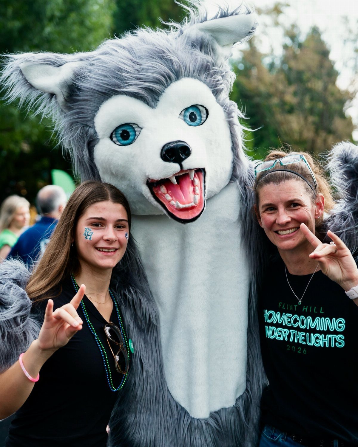 Husky mascot posing with a teenage girl and woman at a homecoming event.