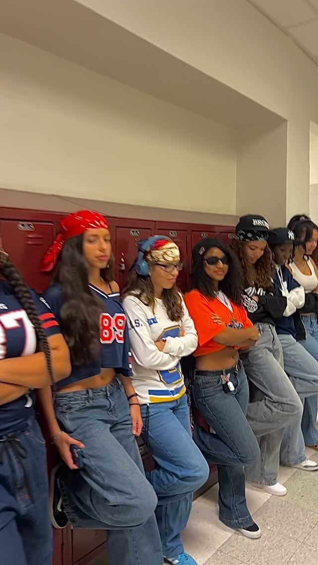 Teenage girls in 90s themed outfits posing against red school lockers in a hallway.