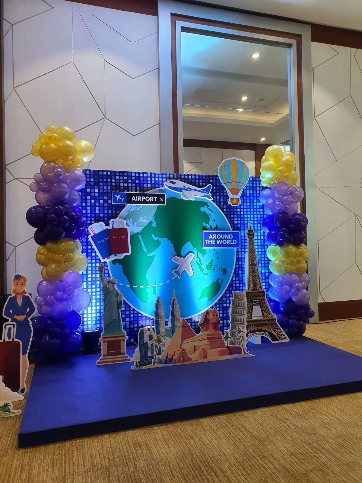 Travel-themed event backdrop with a globe, world landmarks, and colorful balloon columns.