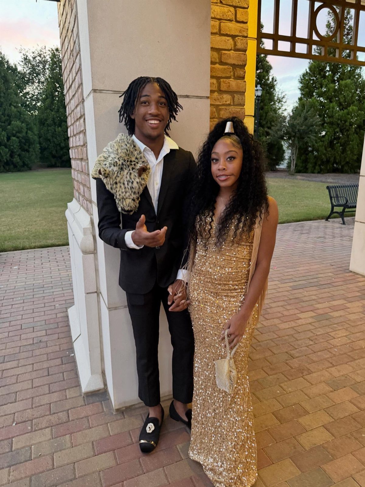 Young couple posing in a black suit and gold sequined gown for homecoming.