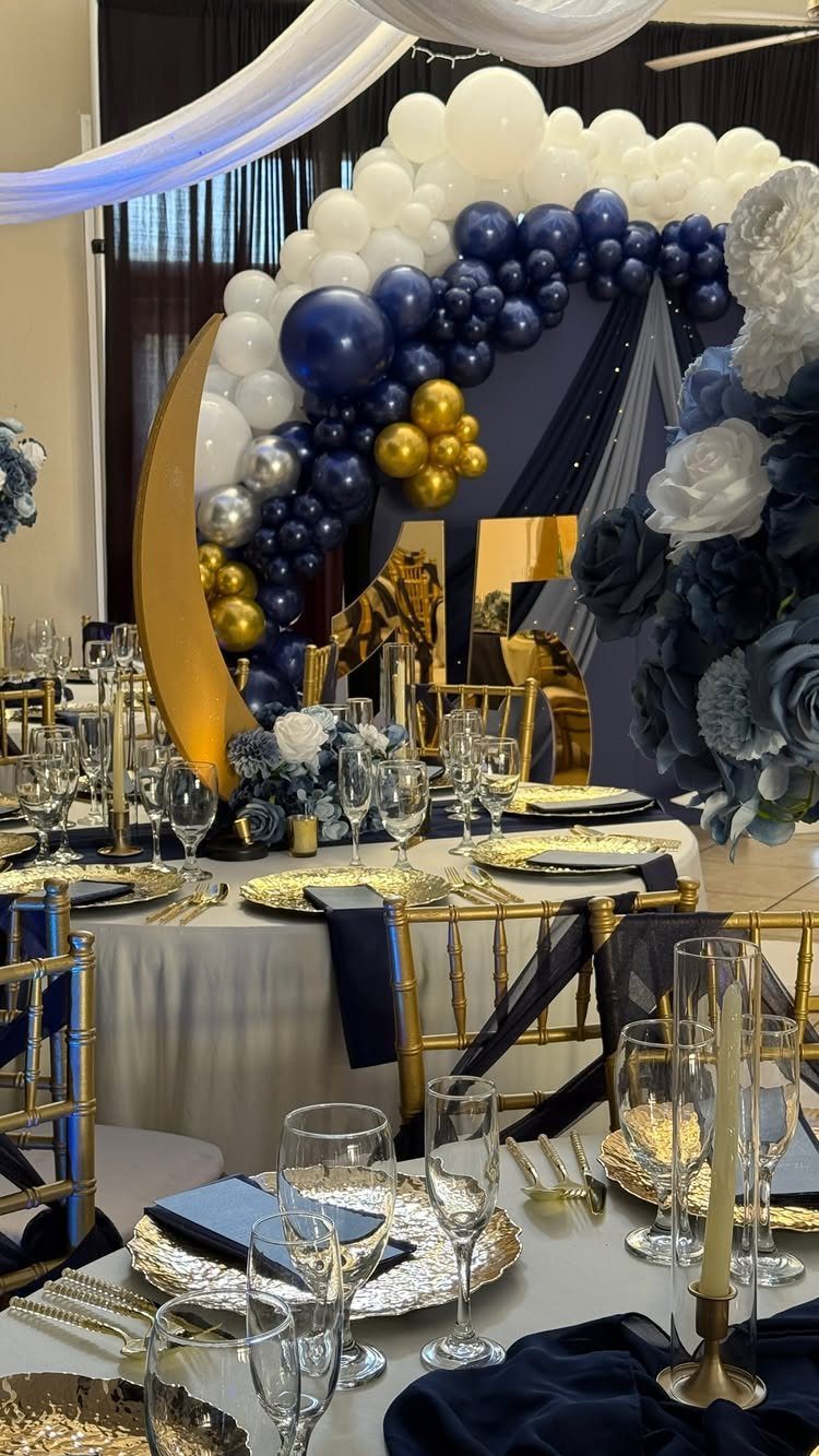 Event tables with gold and navy decor and a large balloon arch backdrop.