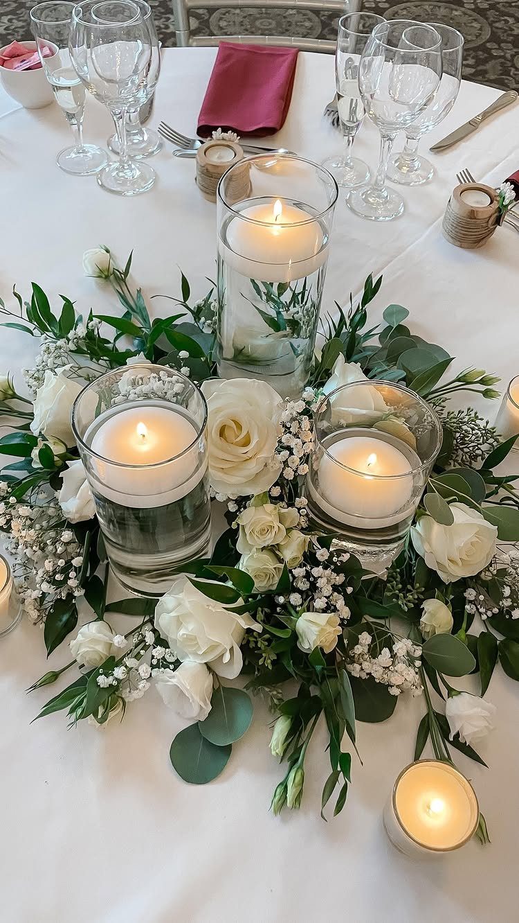 White rose and greenery centerpiece with floating candles on a white table.