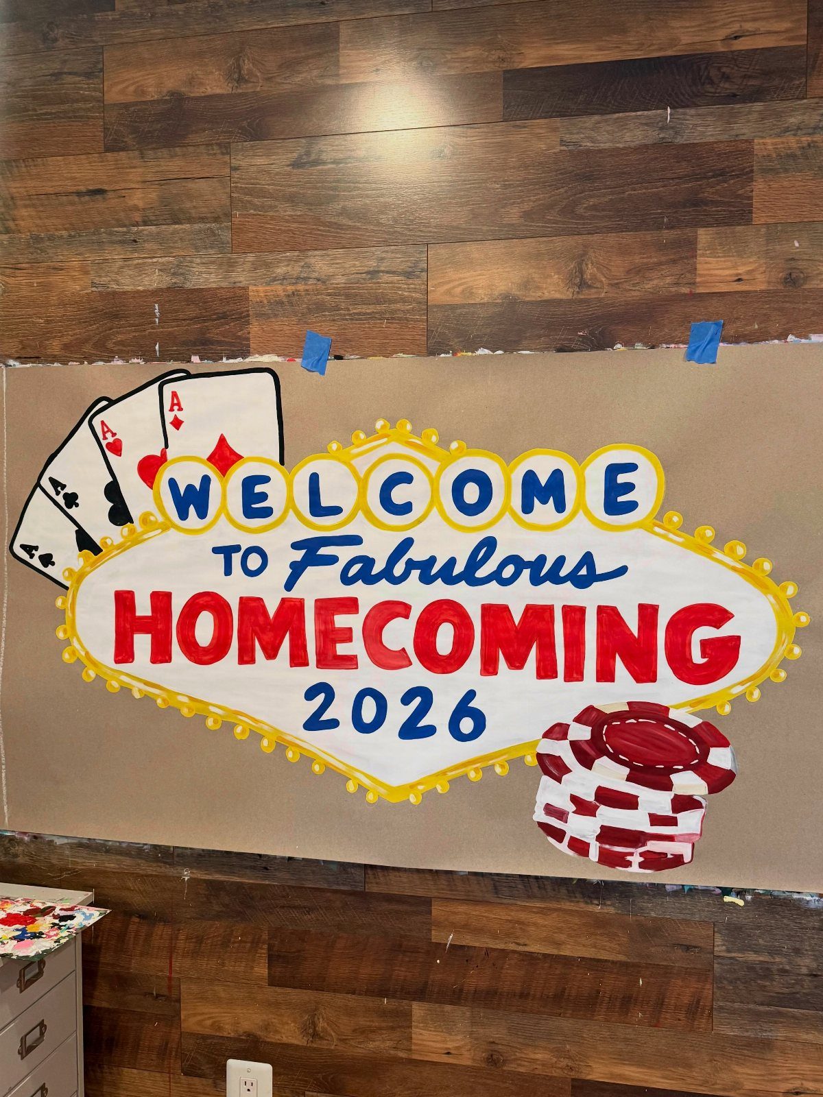 Hand-painted homecoming banner with Las Vegas casino elements on a wood wall
