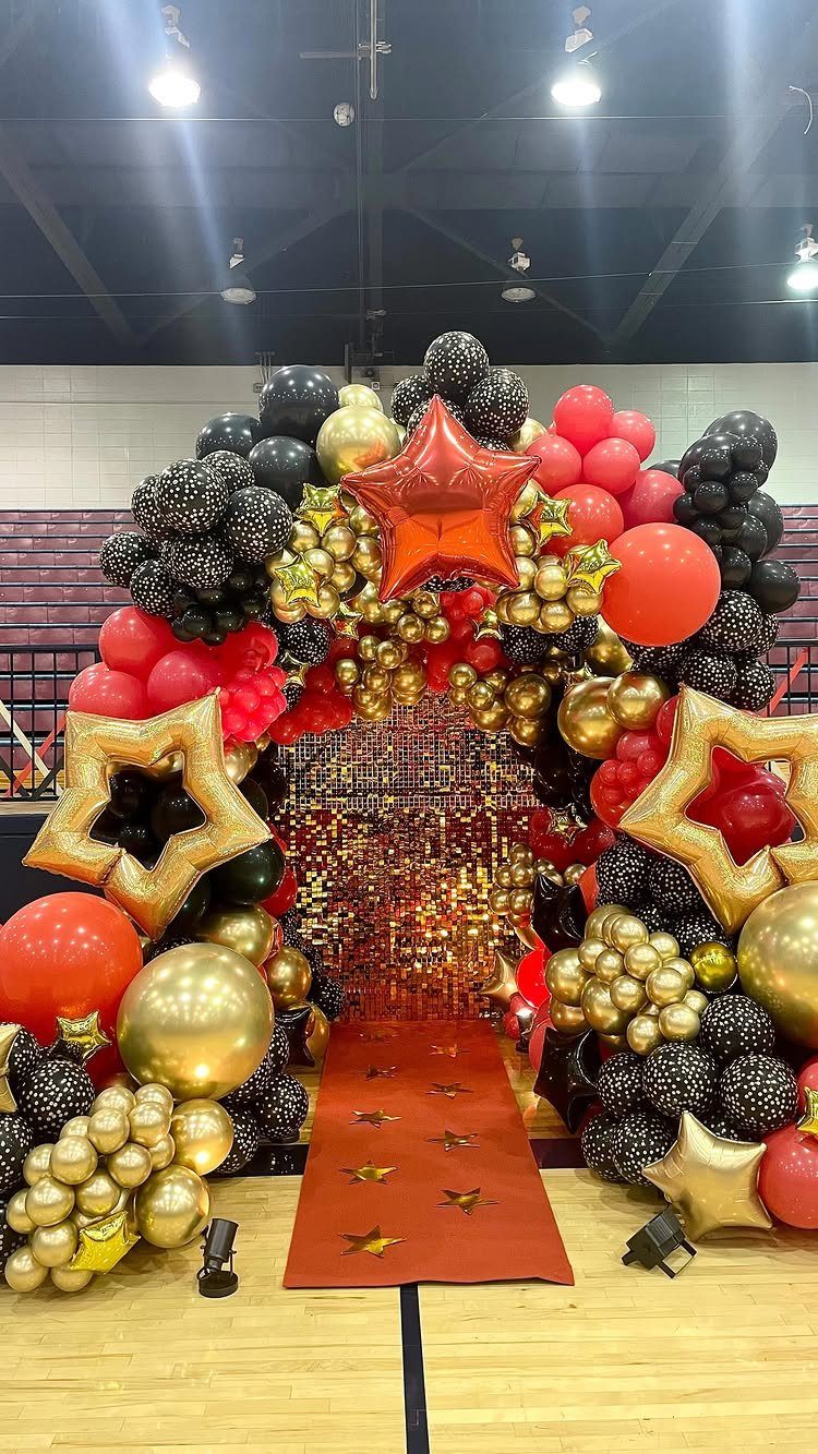Red carpet entrance with a red, gold, and black balloon arch and stars.
