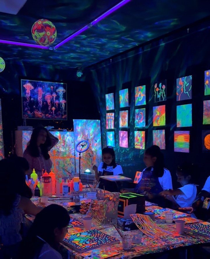 Children painting with neon colors in a dark room with glowing art displays.