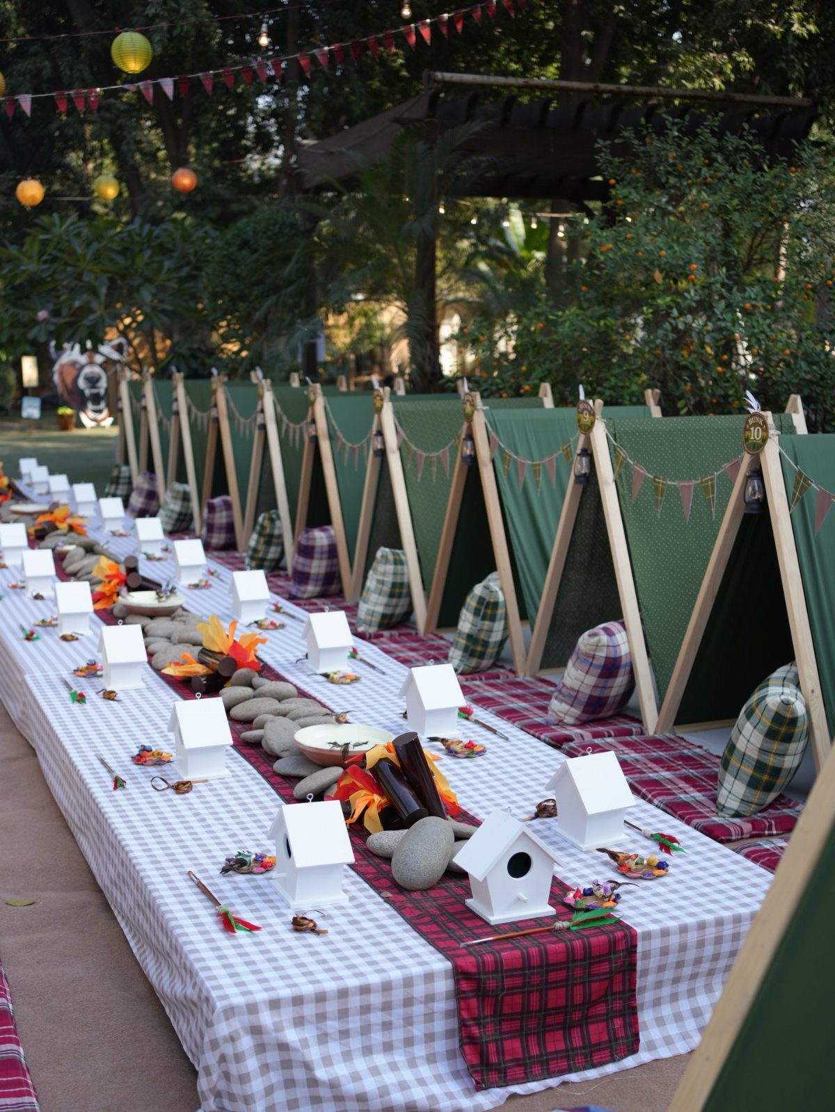 Small green A-frame tents and a decorated long table for a backyard camping party.
