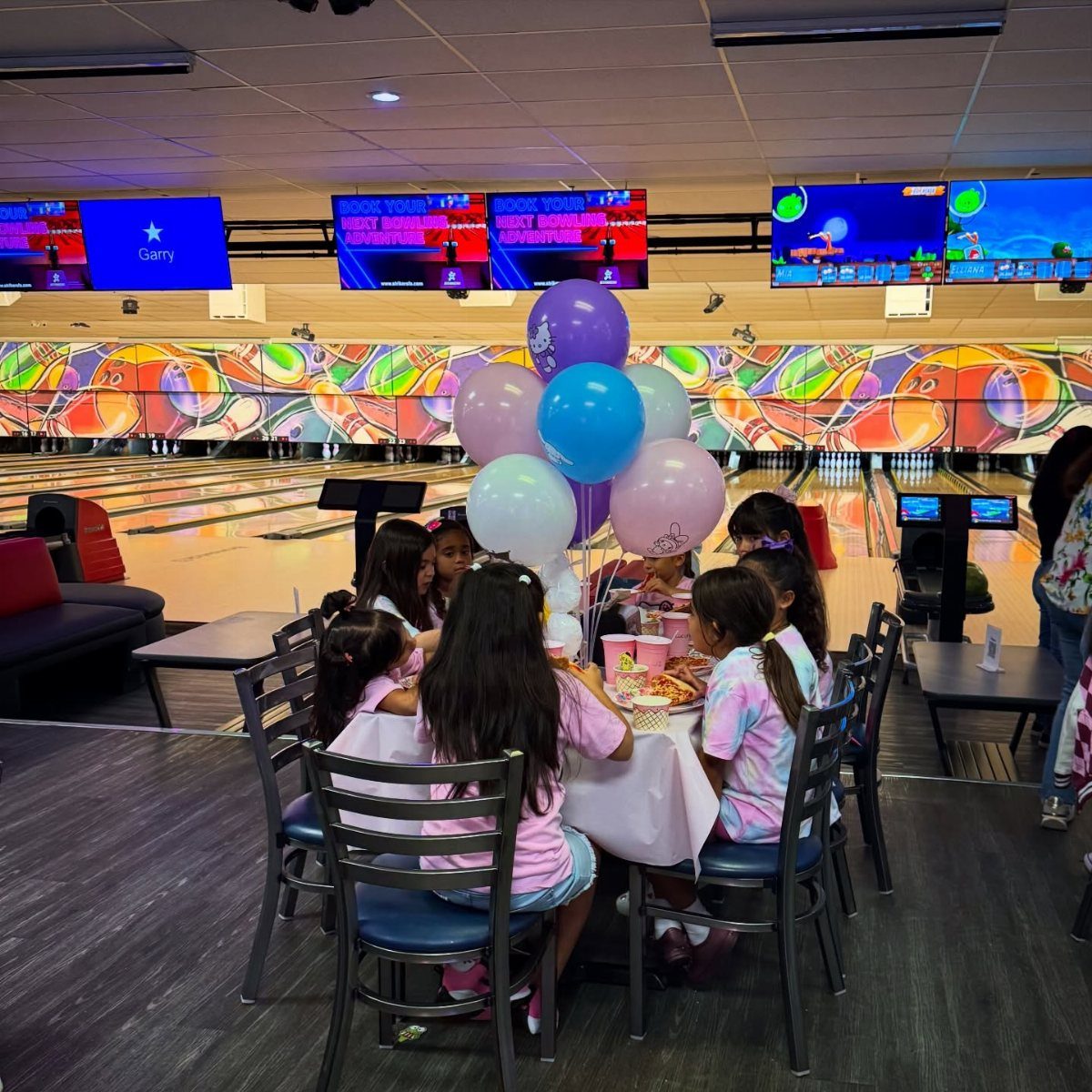Young girls sitting at a decorated table inside a bowling alley for a party.