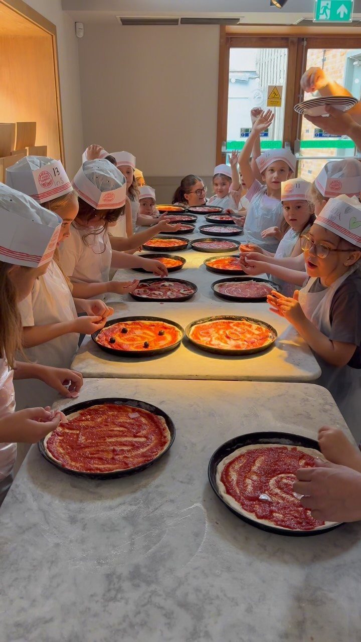 Children in chef hats and aprons making pizzas on a marble counter.