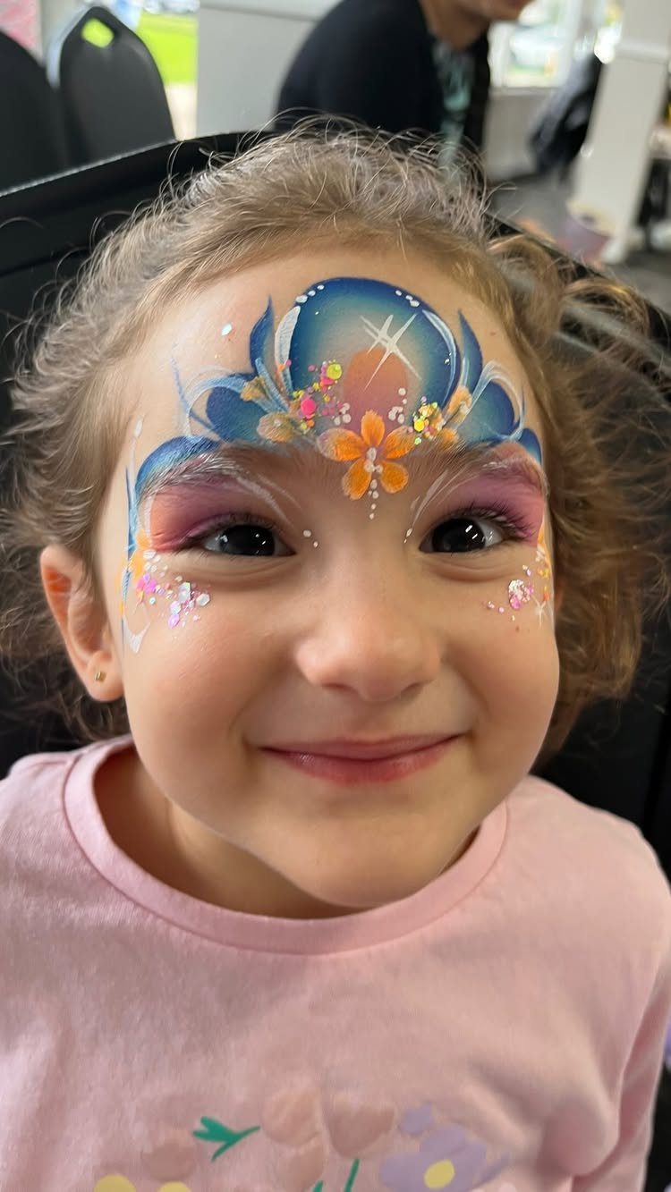 Young girl smiling with colorful glittery face paint and a flower on her forehead