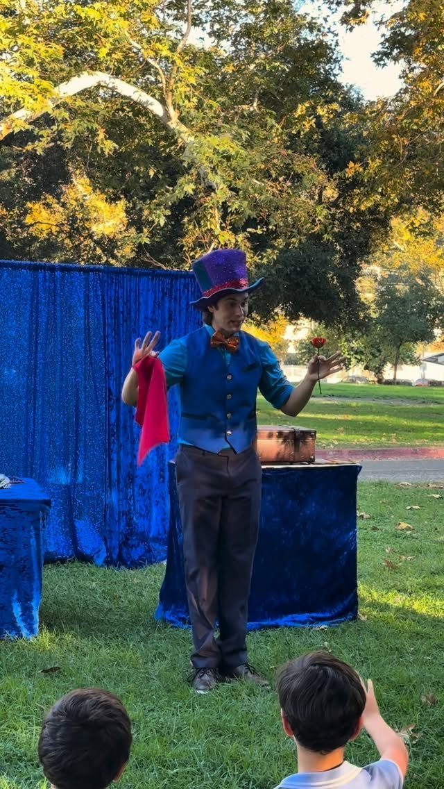 Magician in a purple top hat performing a trick for children outdoors.