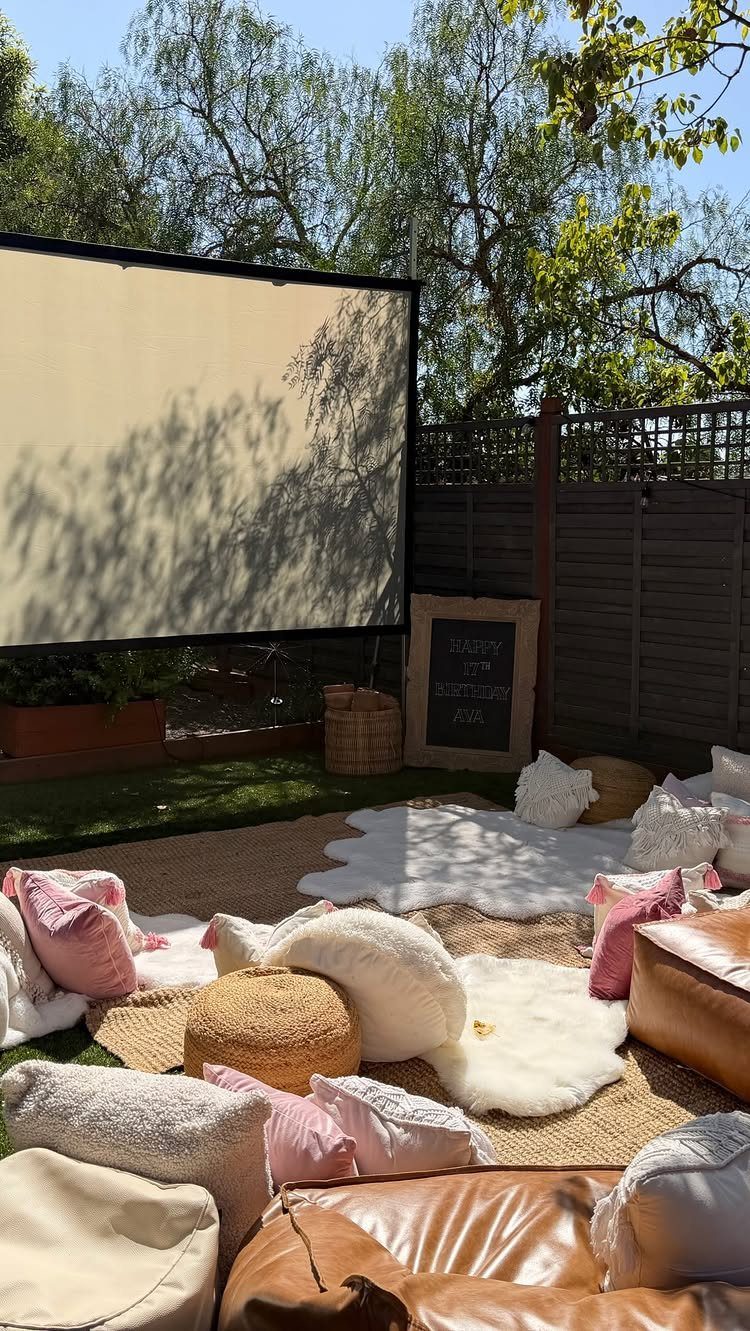 Outdoor movie screen with cozy rugs and pillows on a backyard lawn